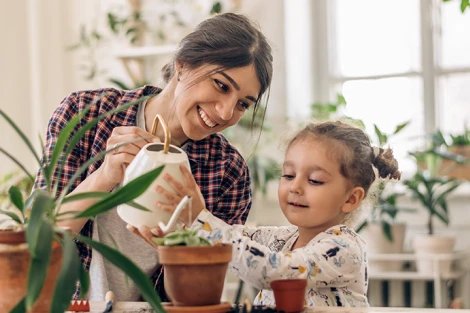 Mother helping her daughter water a house plant