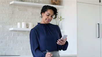 Woman standing at a cafe counter writing while looking at a phone she is holding