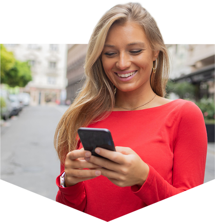 Woman standing outside in the city smiling while looking at phone she is holding